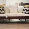 Wooden couch with patterned cushions and blanket.