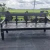 Black bench on wooden deck with greenery.