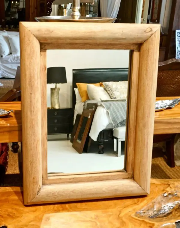 Wooden-framed mirror reflecting a bedroom scene.