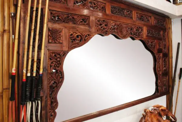 Intricately carved wooden mirror with reflection.