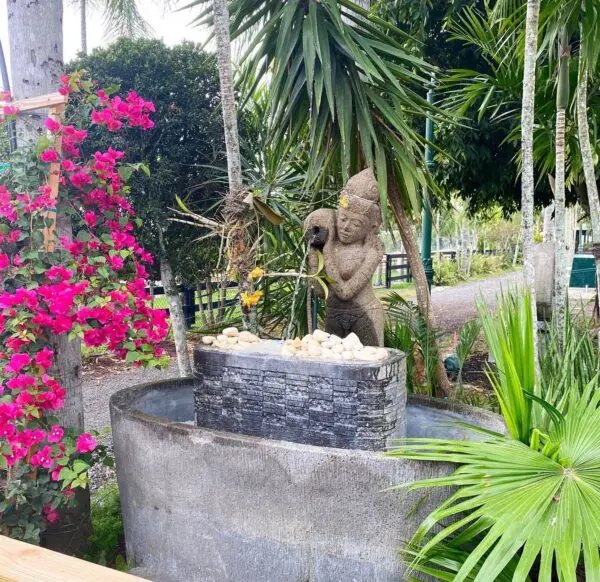 Stone statue next to water fountain and flowers.