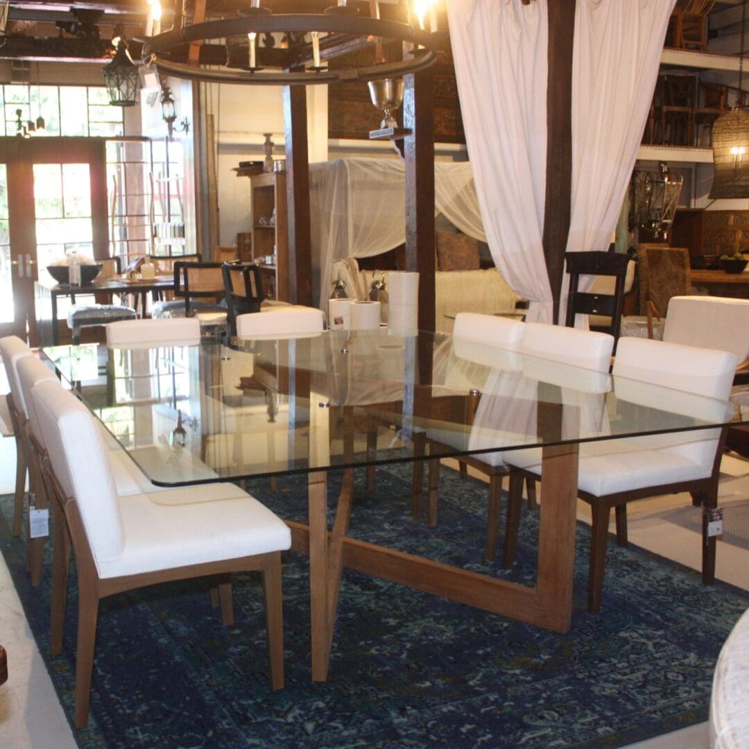 A dining room table with white chairs and a glass top.