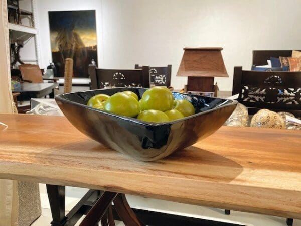 A bowl of green apples on top of a wooden table.