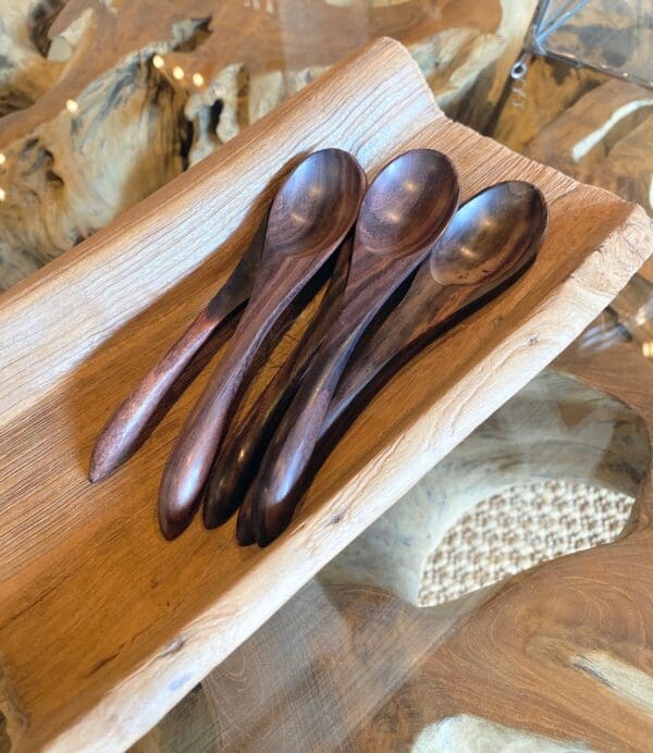 A wooden tray with three spoons on it.